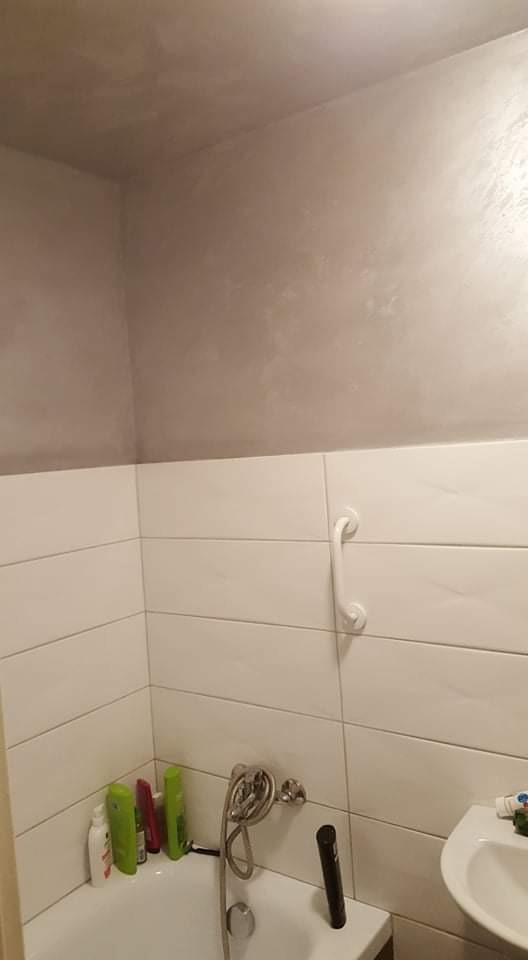 Wykończona łazienka z białymi, poziomymi płytkami, srebrną armaturą i szarą, teksturowaną górną częścią ściany oraz sufitem.