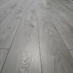 Nowo ułożona, szara podłoga z paneli laminowanych, widok z niskiej perspektywy, z widocznym fragmentem ściany pomalowanej na szaro i zielono.