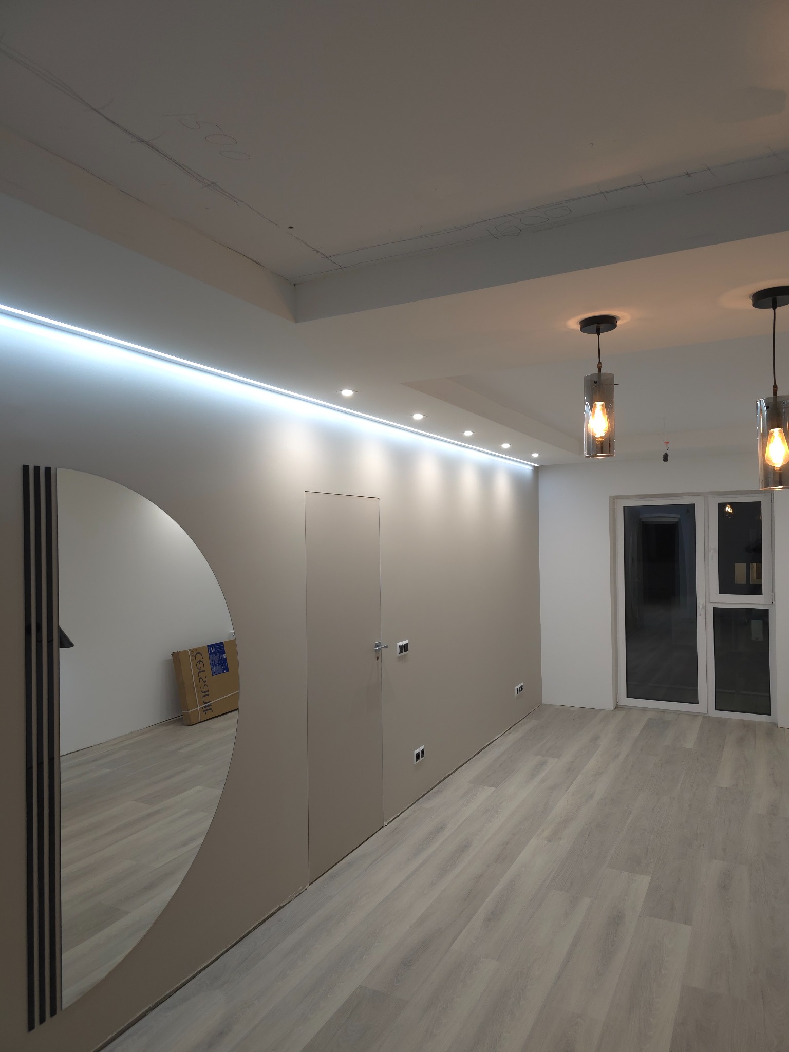 Wykończone wnętrze z szarą podłogą panelową, świeżo pomalowanymi ścianami w odcieniach beżu i bieli, ozdobnym oświetleniem ledowym pod sufitem oraz wiszącymi lampami z żarówkami Edison, duże okno...