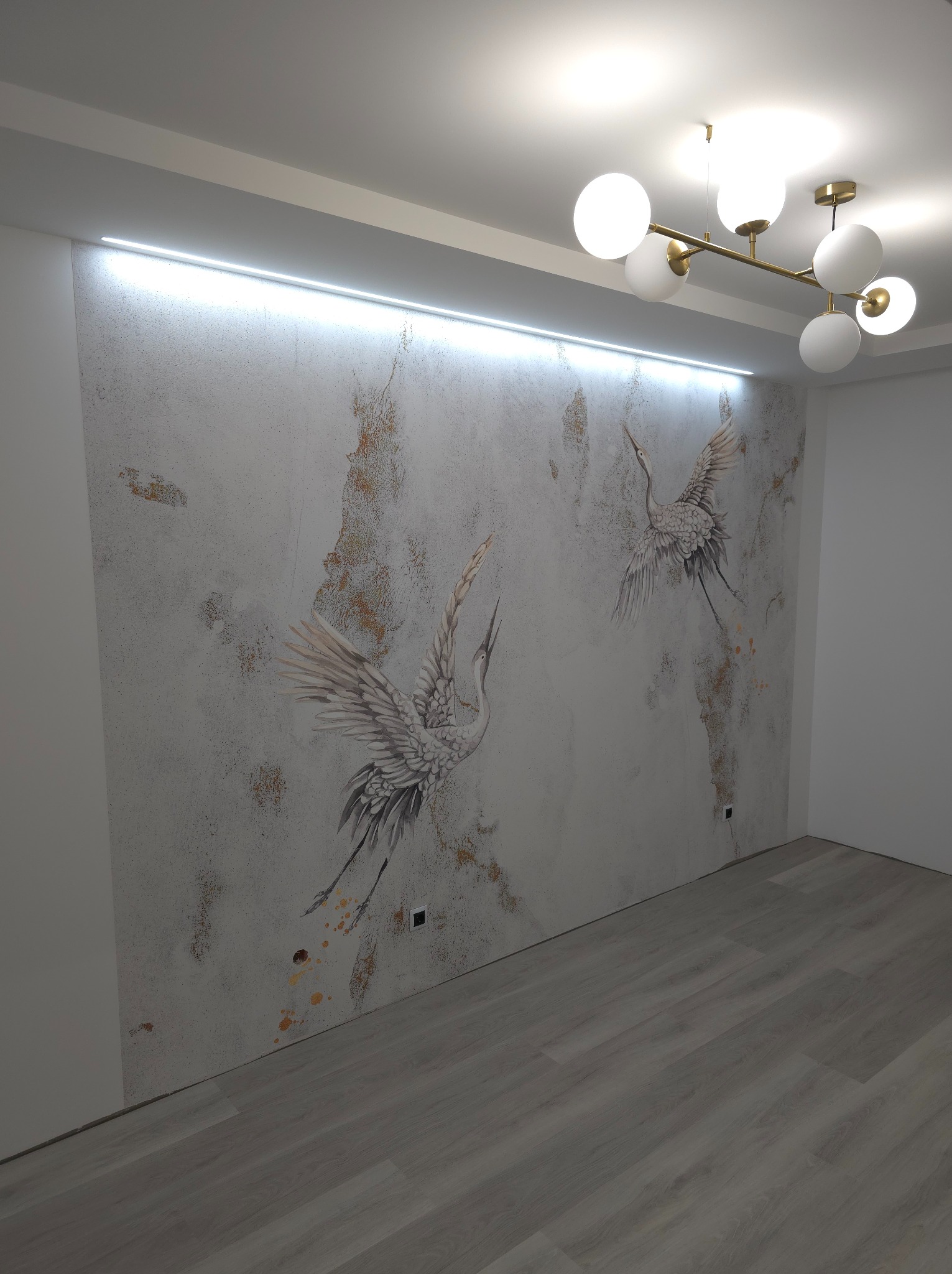 Ściana w pokoju z dekoracyjną fakturą i motywem dwóch żurawi w locie, oświetlona listwą LED pod sufitem i nowoczesną lampą wiszącą z białymi kulami.