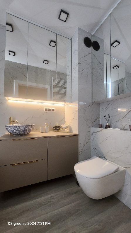 Nowoczesna łazienka wykończona marmurem, z podwieszaną toaletą, szafką z umywalką w stylu retro i dużym lustrem z oświetleniem LED.
