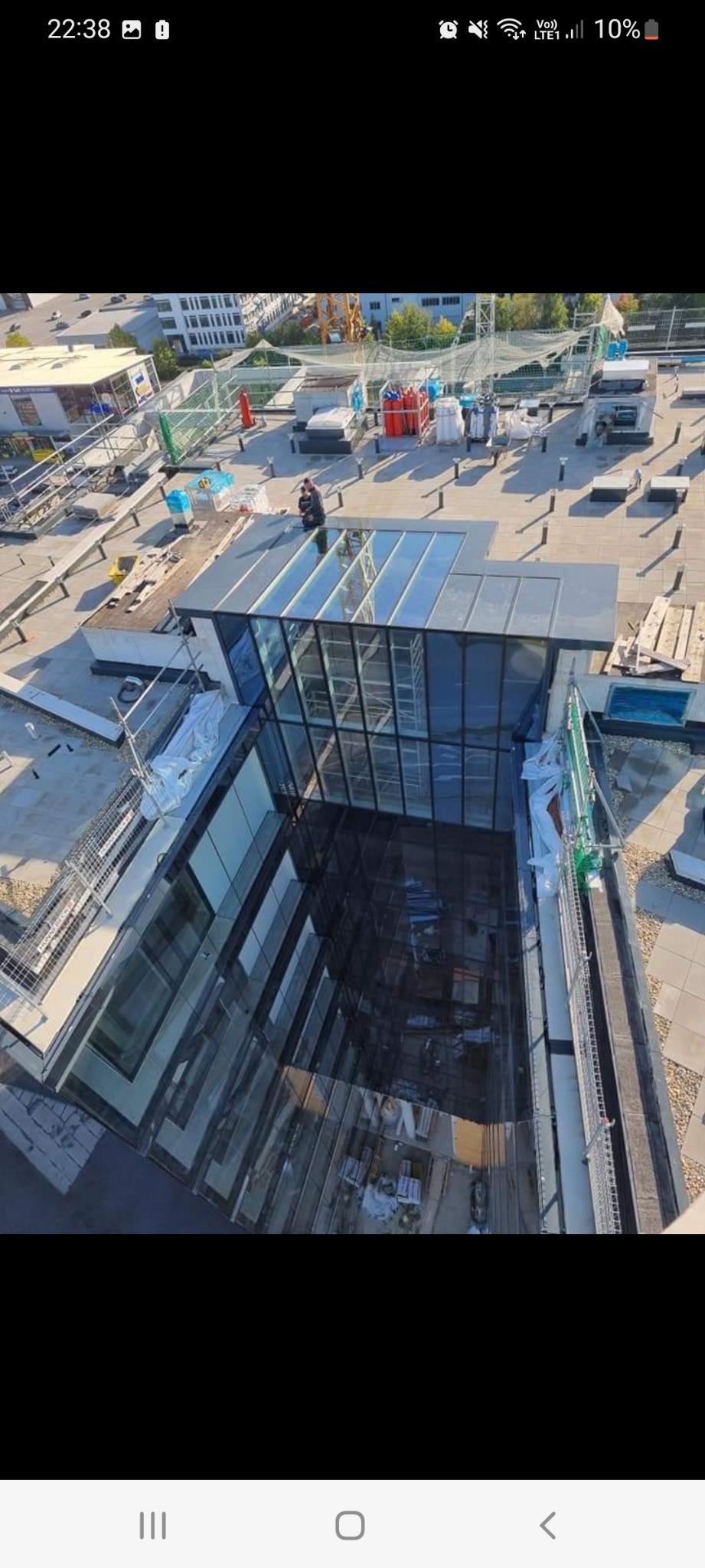 Widok z góry na szklaną konstrukcję okienną w trakcie montażu na dachu budynku, widoczny pracownik oraz materiały budowlane.