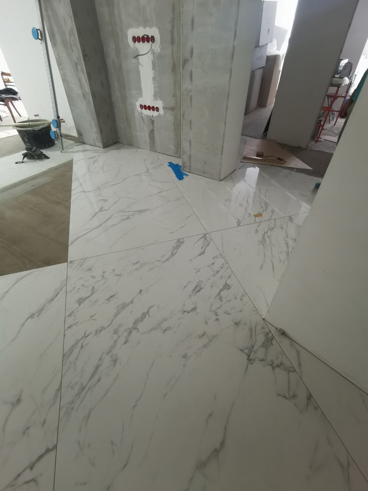 Białe płytki podłogowe z wzorem marmuru, świeżo położone w surowym wnętrzu z widocznymi przewodami elektrycznymi i nieotynkowanymi ścianami.