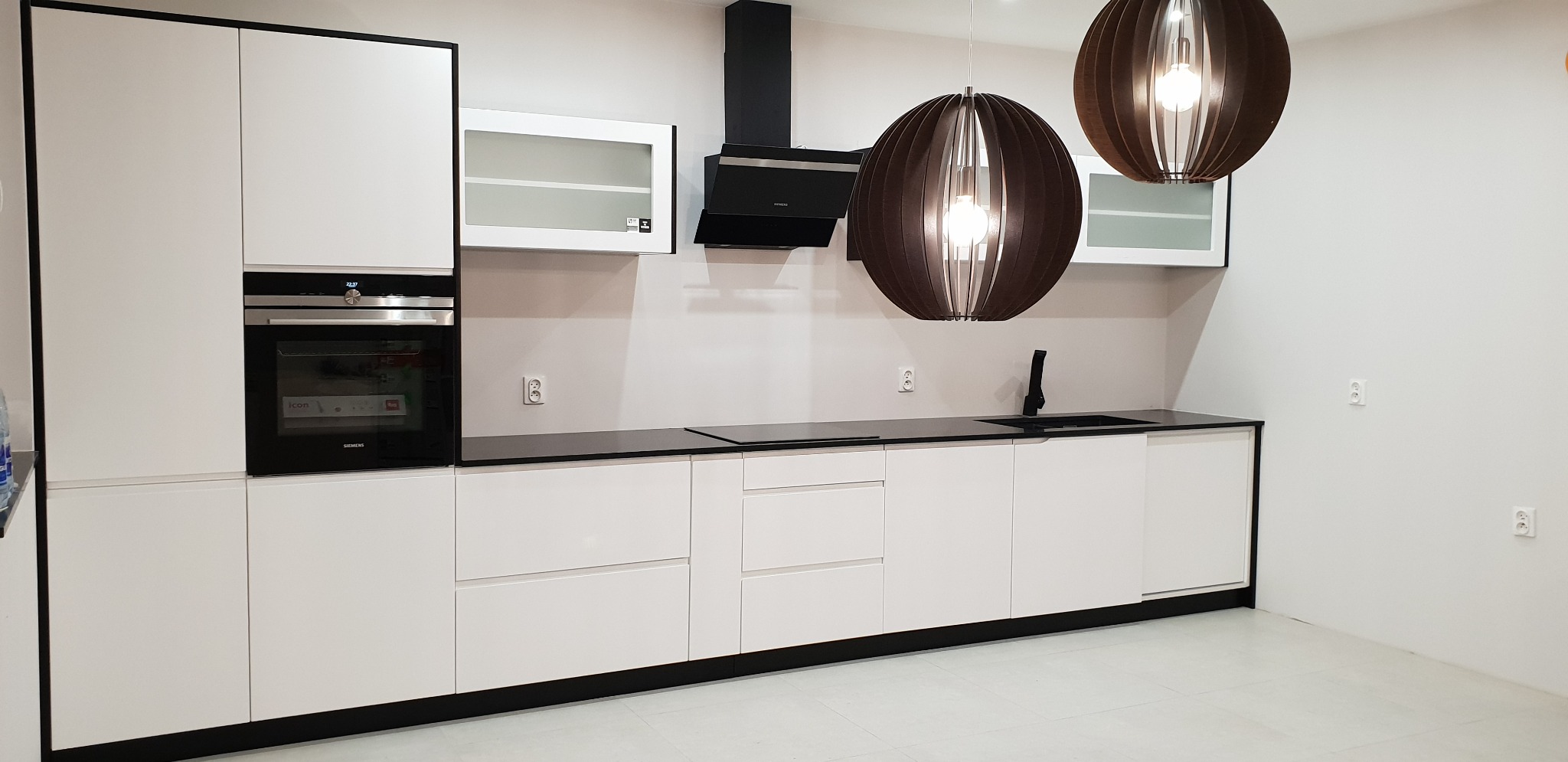 Minimalistyczna kuchnia z białymi szafkami i czarnym blatem we Wrocławiu, oświetlona dekoracyjnymi lampami wiszącymi i wyposażona w piekarnik Siemens oraz czarny okap.