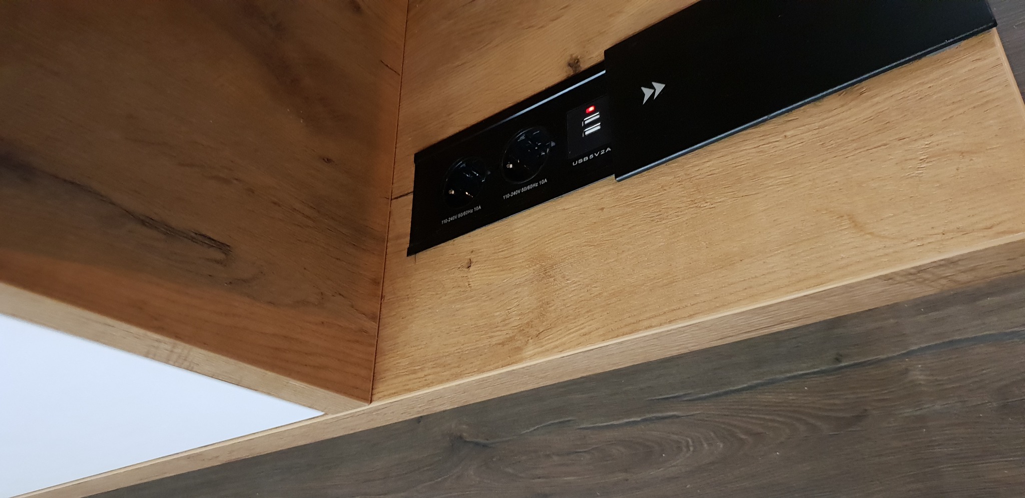 Wpuszczane gniazdo elektryczne z portami USB zamontowane w drewnianej szafce z blatem imitującym drewno.