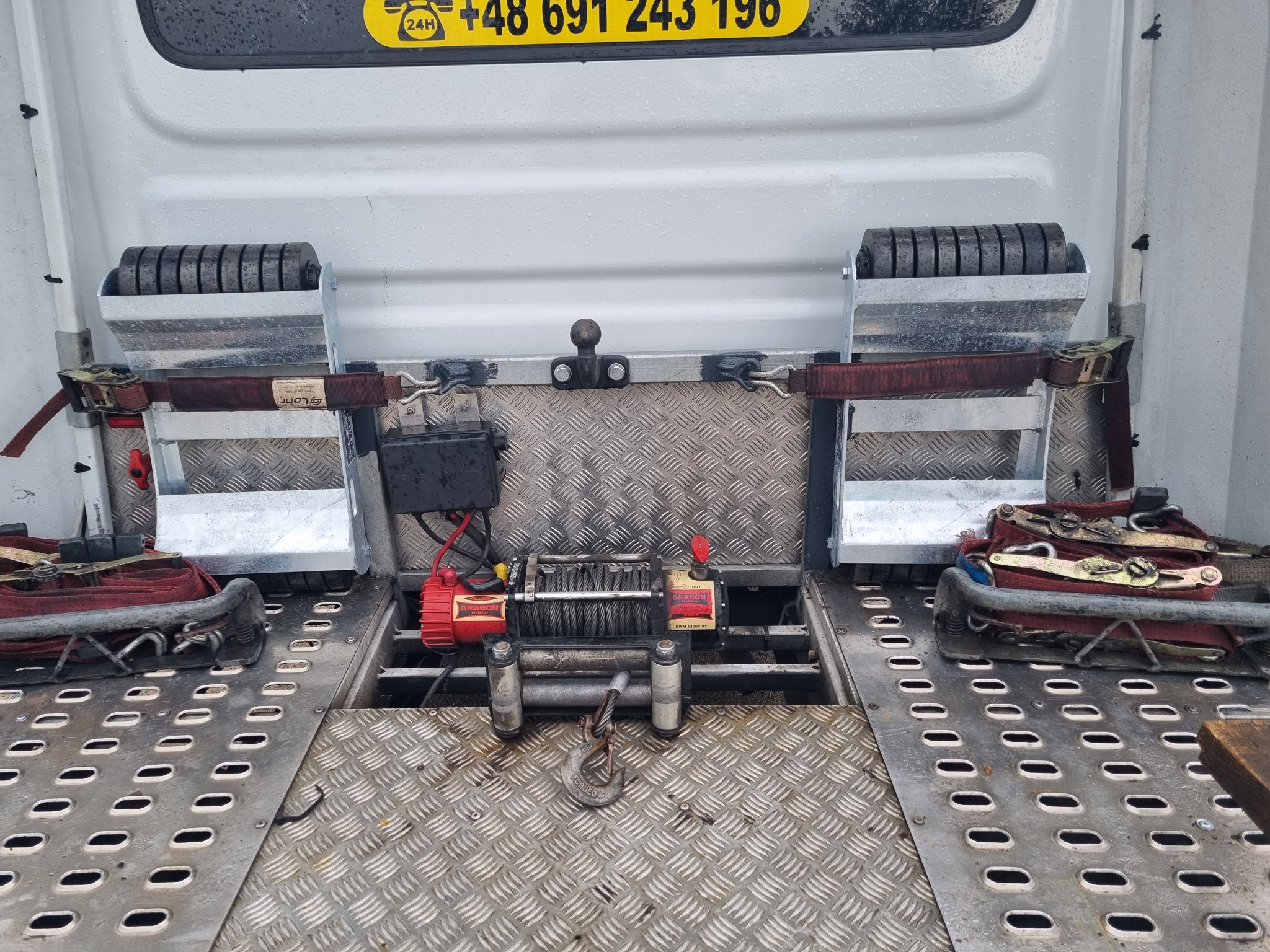 Widok na platformę lawety z zamontowaną wyciągarką Dragon Winch DWM 13000 ST, rolkami najazdowymi i pasami mocującymi, przygotowaną do załadunku pojazdu.