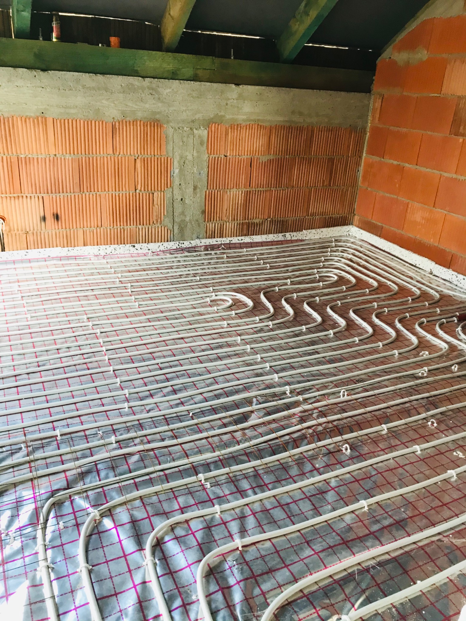 Układ rur grzewczych na folii izolacyjnej z siatką, przygotowany do wylewki w pomieszczeniu z surowymi ścianami z cegły.