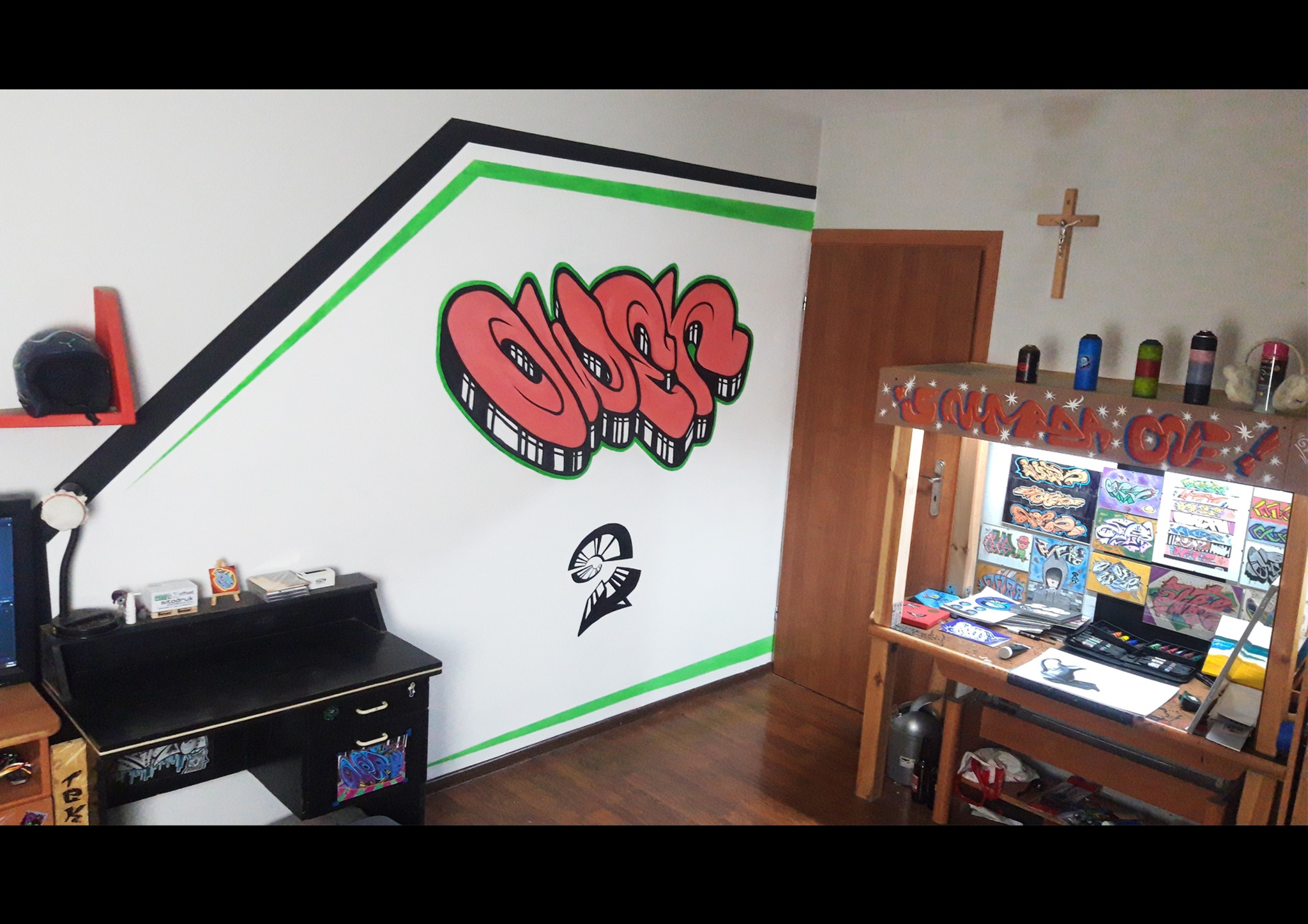 Pokój z graffiti na ścianie: czerwony napis w stylu 3D z czarną obwódką, czarny symbol poniżej, czarno-zielone pasy na górze ściany, biurko z akcesoriami artystycznymi i szkicami.