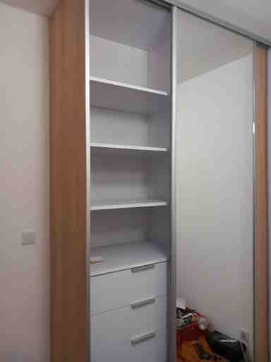 Wnętrze szafy z przesuwnymi drzwiami, widoczne półki, szuflady z metalowymi uchwytami i bałagan na podłodze wewnątrz szafy.