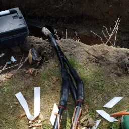 Kable energetyczne z miedzianymi żyłami wystające z wykopu w Jakubowie, widoczne narzędzia i resztki izolacji.