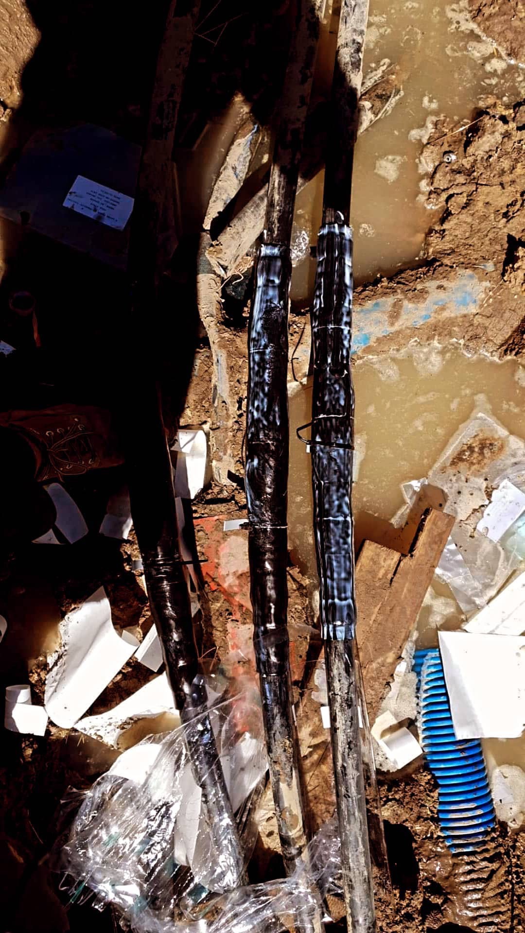 Podziemne kable elektryczne połączone mufami zalane wodą w wykopie, widoczne ślady błota i resztki materiałów izolacyjnych.