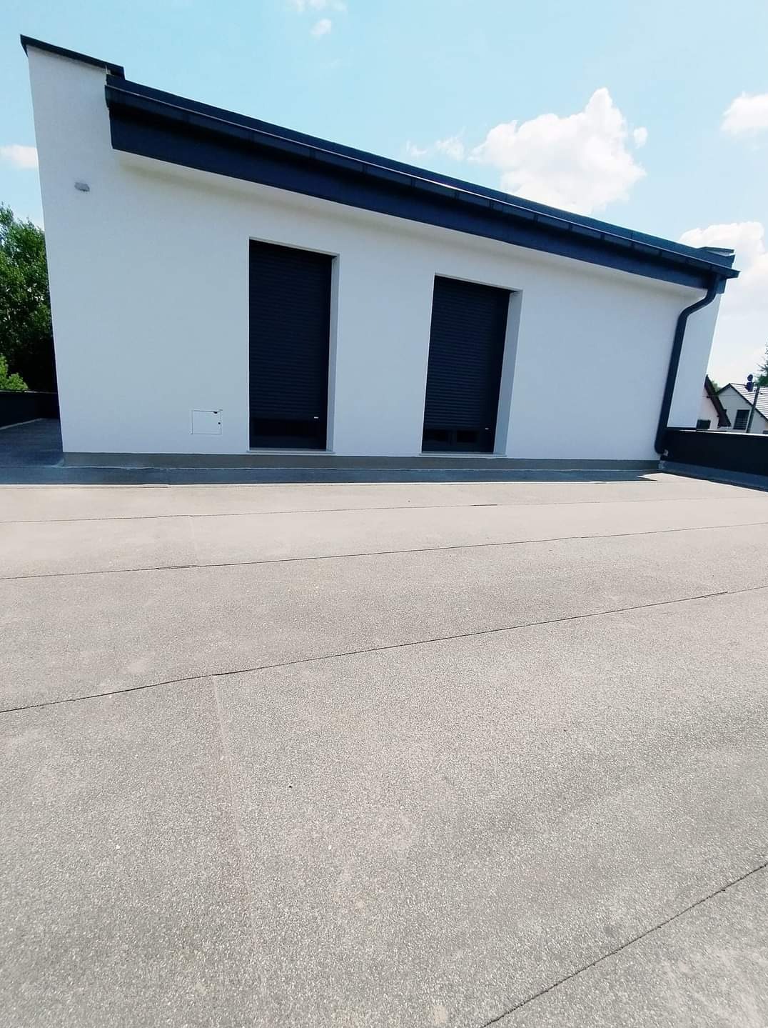 Nowoczesny budynek z białymi ścianami, czarnym dachem i roletami zewnętrznymi, widok z poziomu dachu.