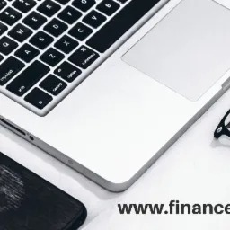 Laptop, okulary i telefon na białym biurku, sugerujące pracę biurową lub zdalną.