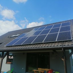 EMPA Sp z o.o - Dom z ciemną dachówką i panelami słonecznymi na dachu, widok z dołu na tle błękitnego nieba z chmurami.