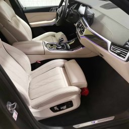 Monkey Showers - Wnętrze luksusowego samochodu BMW z jasną skórzaną tapicerką, widoczne fotele z elektryczną regulacją, deska rozdzielcza z podświetleniem ambientowym i logo M na progu.