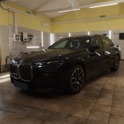 Monkey Showers - Czarny samochód BMW serii 7 po umyciu w jasnej myjni, widoczne mokre płytki na podłodze i ślady wody na lakierze.