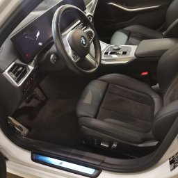 Monkey Showers - Wnętrze samochodu BMW z czarną skórzaną tapicerką i elementami z włókna węglowego, widok z otwartych drzwi.