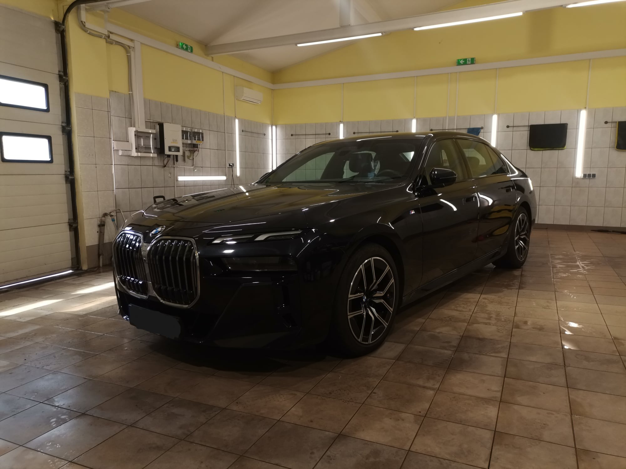 Czarny samochód BMW serii 7 po umyciu w jasnej myjni, widoczne mokre płytki na podłodze i ślady wody na lakierze.