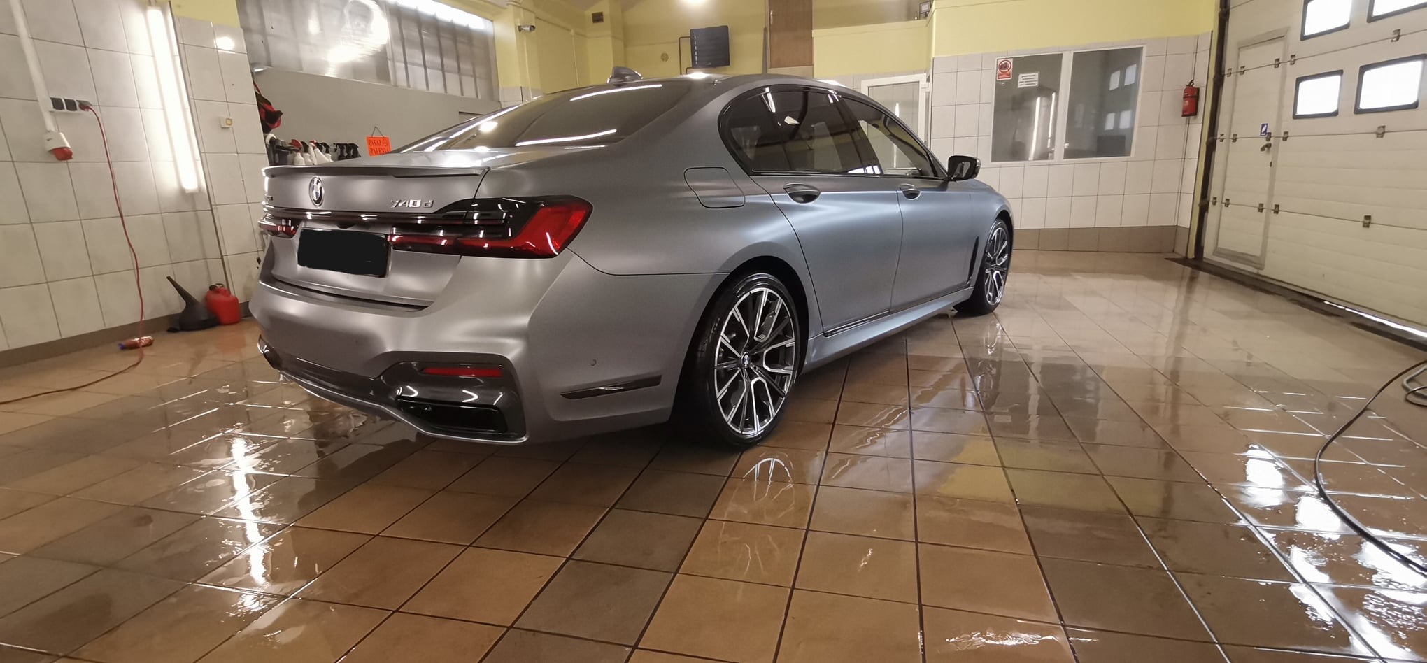 Szary samochód BMW serii 7 po umyciu, z widocznymi kroplami wody na lakierze i mokrej podłodze w myjni.