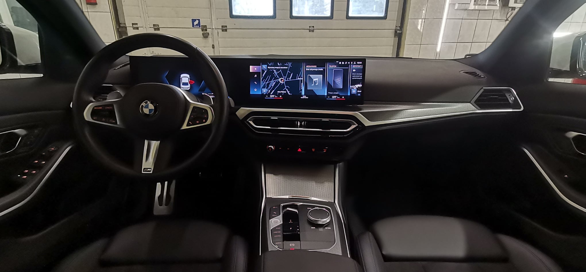 Wnętrze nowoczesnego samochodu BMW z widocznym kokpitem, kierownicą i ekranem nawigacji, srebrne akcenty na desce rozdzielczej