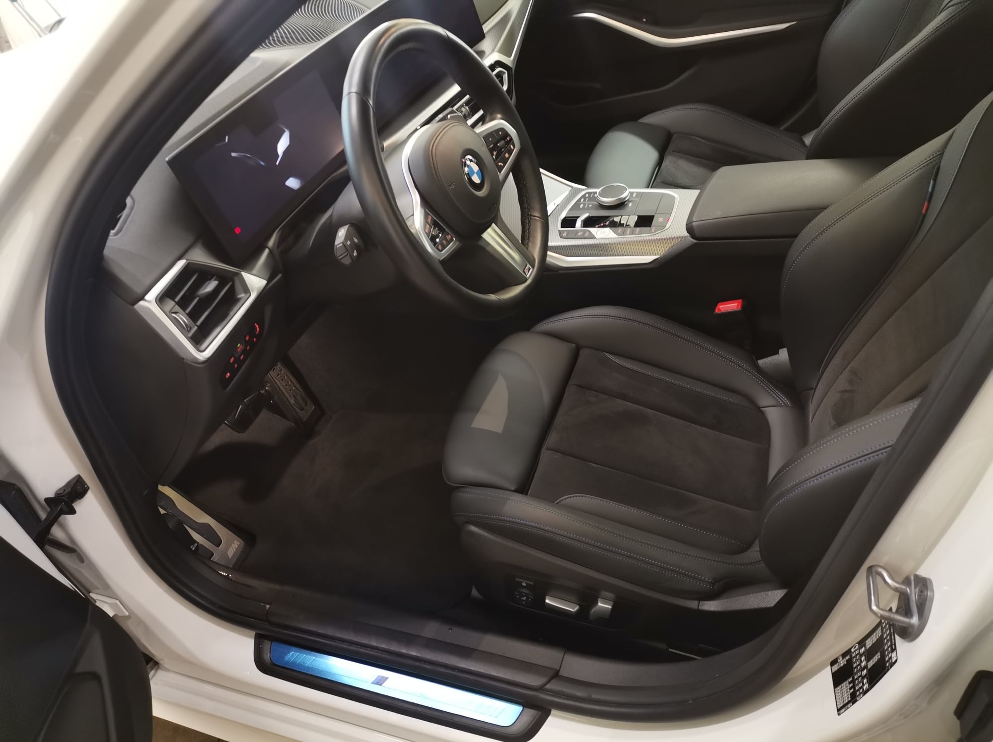 Wnętrze samochodu BMW z czarną skórzaną tapicerką i elementami z włókna węglowego, widok z otwartych drzwi.