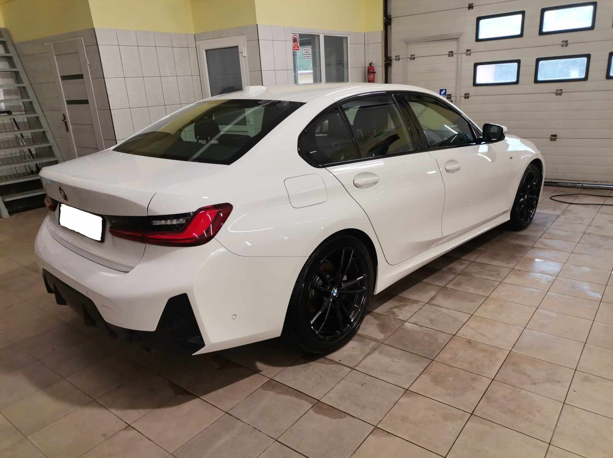 Białe BMW serii 3 po umyciu, z czarnymi felgami, stojące w jasnym pomieszczeniu z kafelkami na podłodze i ścianach.