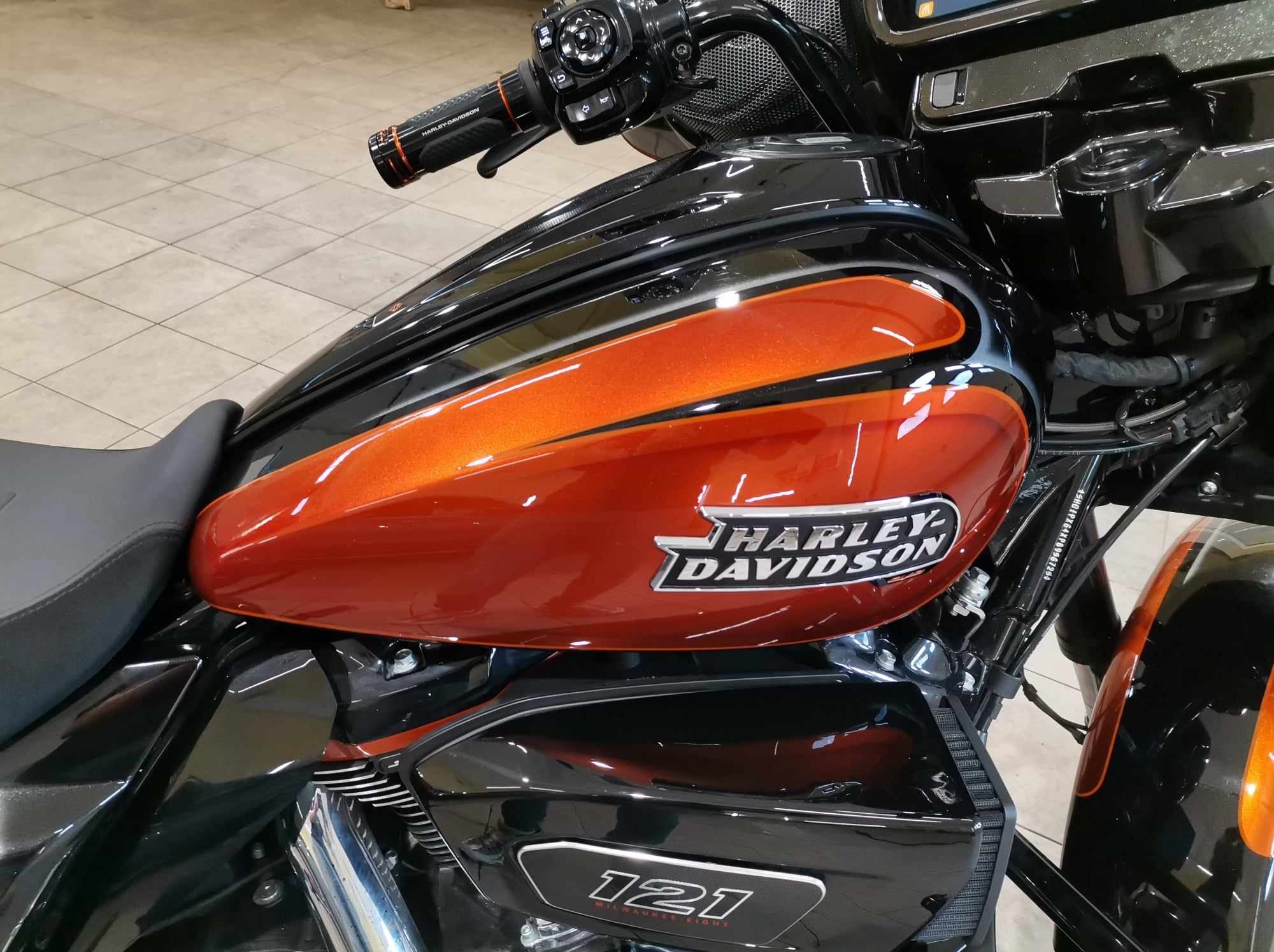Błyszczący, pomarańczowo-czarny zbiornik paliwa motocykla Harley-Davidson z widocznym logo i oznaczeniem silnika 121 Milwaukee Eight.