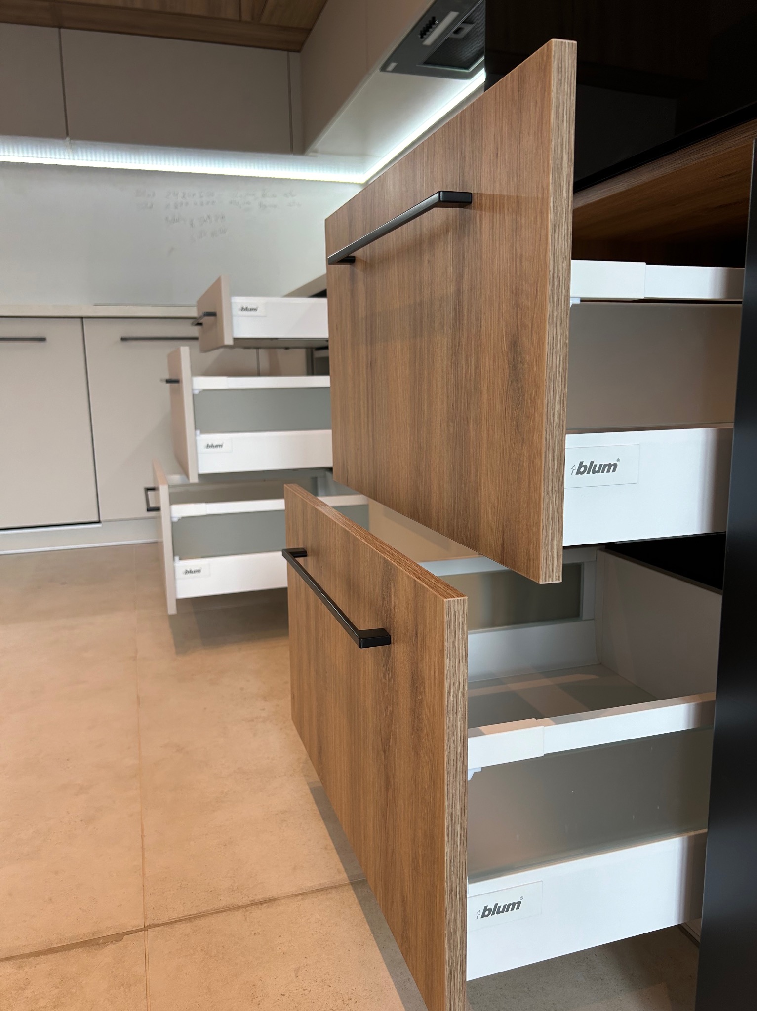 Wysuwane szuflady z drewnianymi frontami i czarnymi uchwytami w nowoczesnej kuchni, widoczne białe wnętrza szuflad z logo Blum.