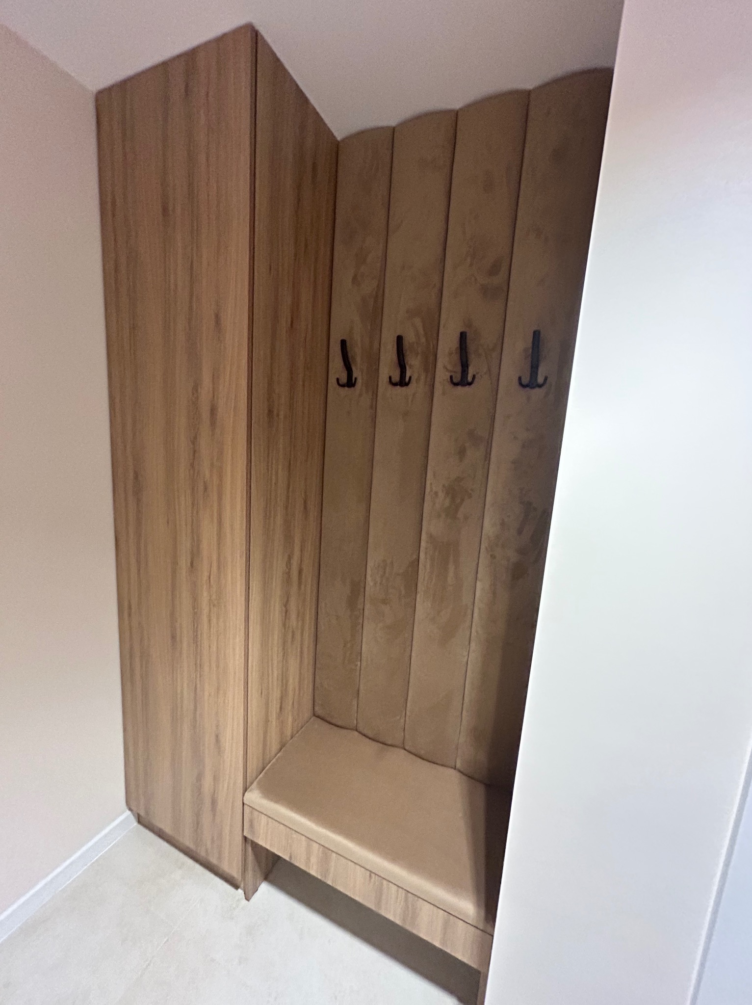 Wnęka z siedziskiem i wieszakami, obok szafa w odcieniach beżu i brązu, całość wkomponowana w przedpokój.