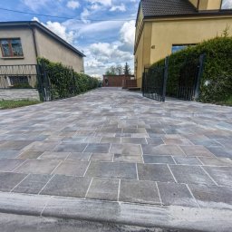 KAR-BRUK KAROL PAPROCKI - Szeroki, brukowany podjazd z kostki w odcieniach szarości i beżu, prowadzący do otwartej bramy i domu z numerem 42. Po bokach metalowe ogrodzenia i zieleń.
