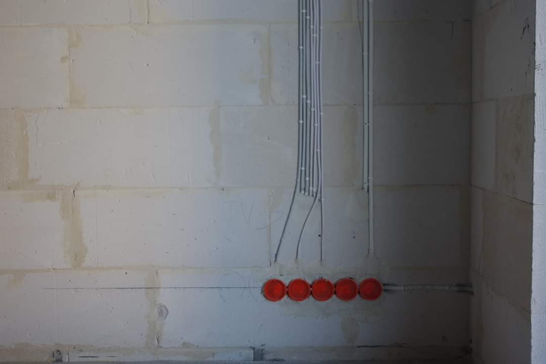 Surowa ściana z betonu komórkowego z wyprowadzonymi przewodami elektrycznymi i pomarańczowymi puszkami instalacyjnymi w rzędzie.