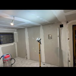 REMMAR - Wnętrze w trakcie montażu płyt gipsowo-kartonowych, widoczny odkurzacz przemysłowy i lampa halogenowa na statywie.