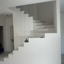 REMMAR - Nowoczesne, białe schody spiralne w minimalistycznym wnętrzu, świeżo po malowaniu, z widocznymi akcesoriami malarskimi na jednym ze stopni.