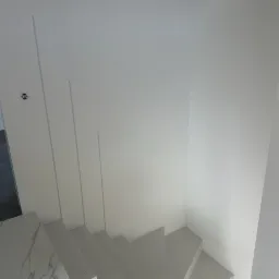 Nowoczesne, białe schody z marmurowym podestem, widok z góry, minimalistyczne wykończenie ścian z subtelnymi pionowymi wgłębieniami.