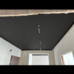 REMMAR - Pomieszczenie w trakcie prac wykończeniowych, sufit pomalowany na czarno, ściany w kolorze białym, widoczne przewody elektryczne.