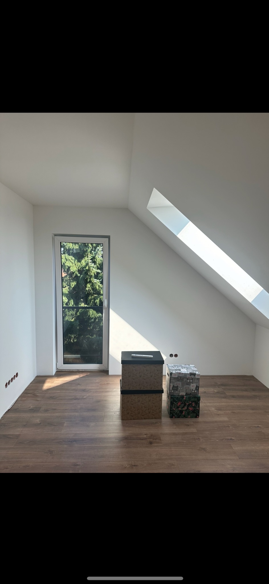 Poddasze po remoncie z drewnianą podłogą, świeżo pomalowanymi białymi ścianami i oknem dachowym, z dwoma pudełkami na środku pokoju