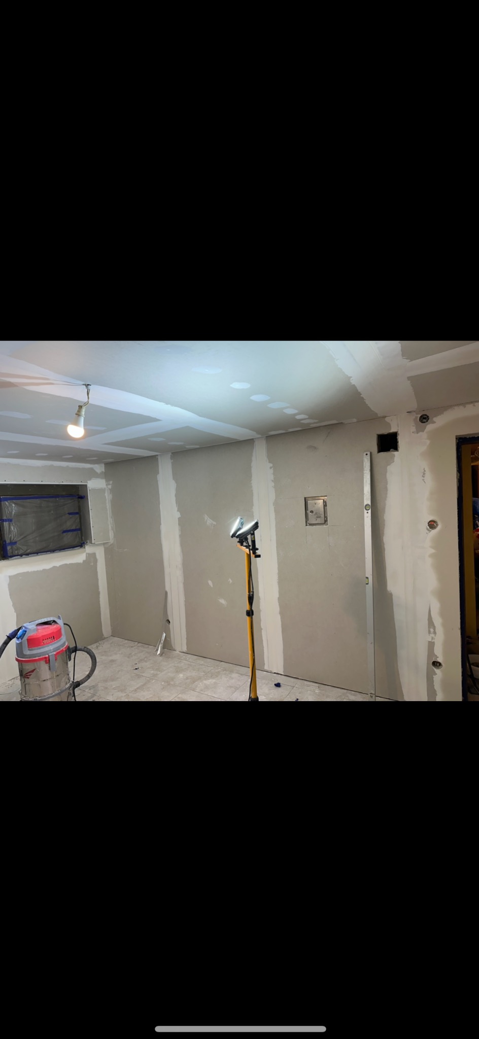 Wnętrze w trakcie montażu płyt gipsowo-kartonowych, widoczny odkurzacz przemysłowy i lampa halogenowa na statywie.