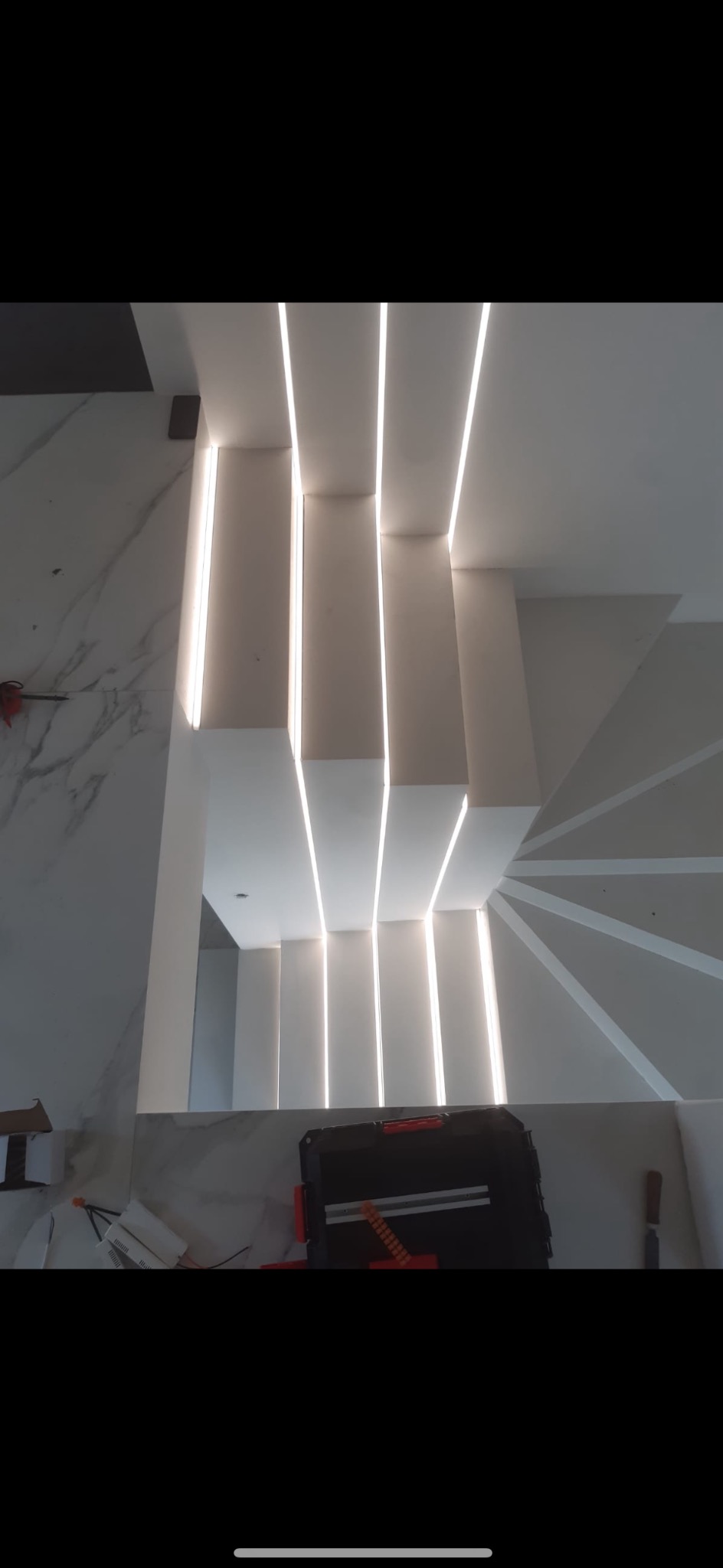 Nowoczesne schody z podświetleniem LED z góry, widoczna skrzynka narzędziowa i fragment marmurowej ściany