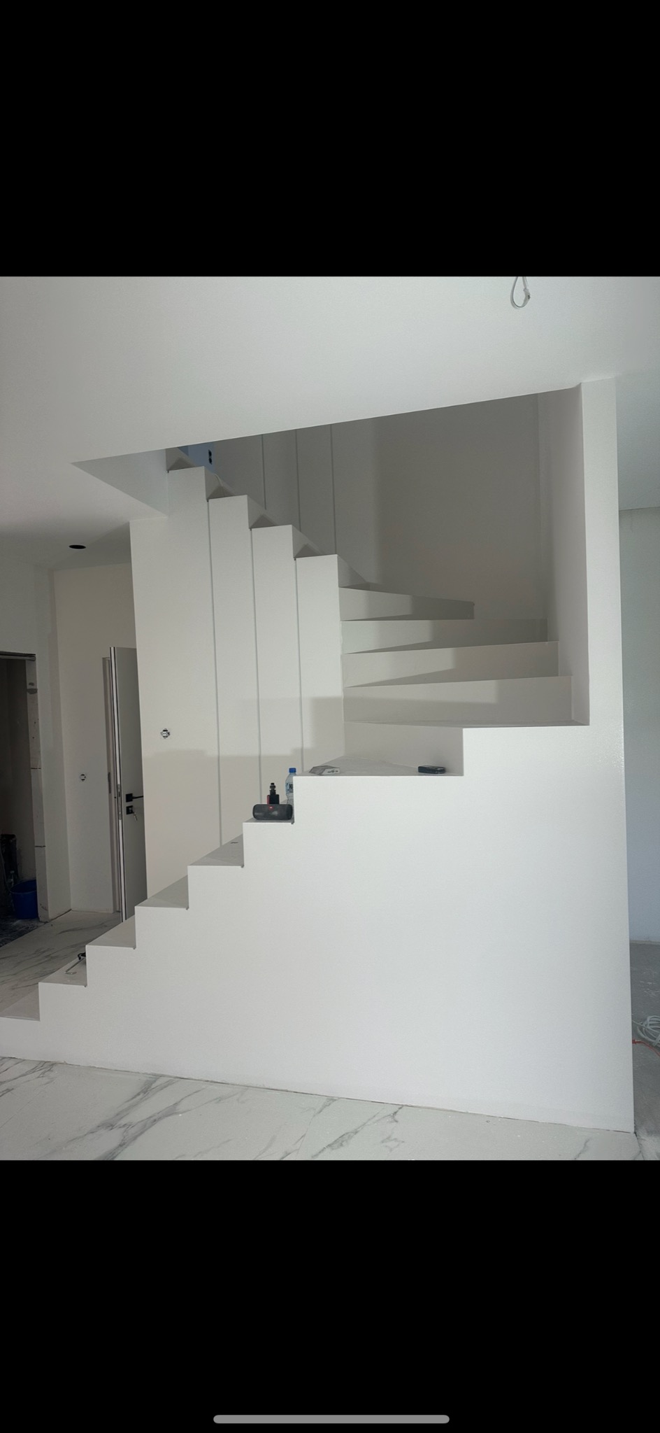 Nowoczesne, białe schody spiralne w minimalistycznym wnętrzu, świeżo po malowaniu, z widocznymi akcesoriami malarskimi na jednym ze stopni.