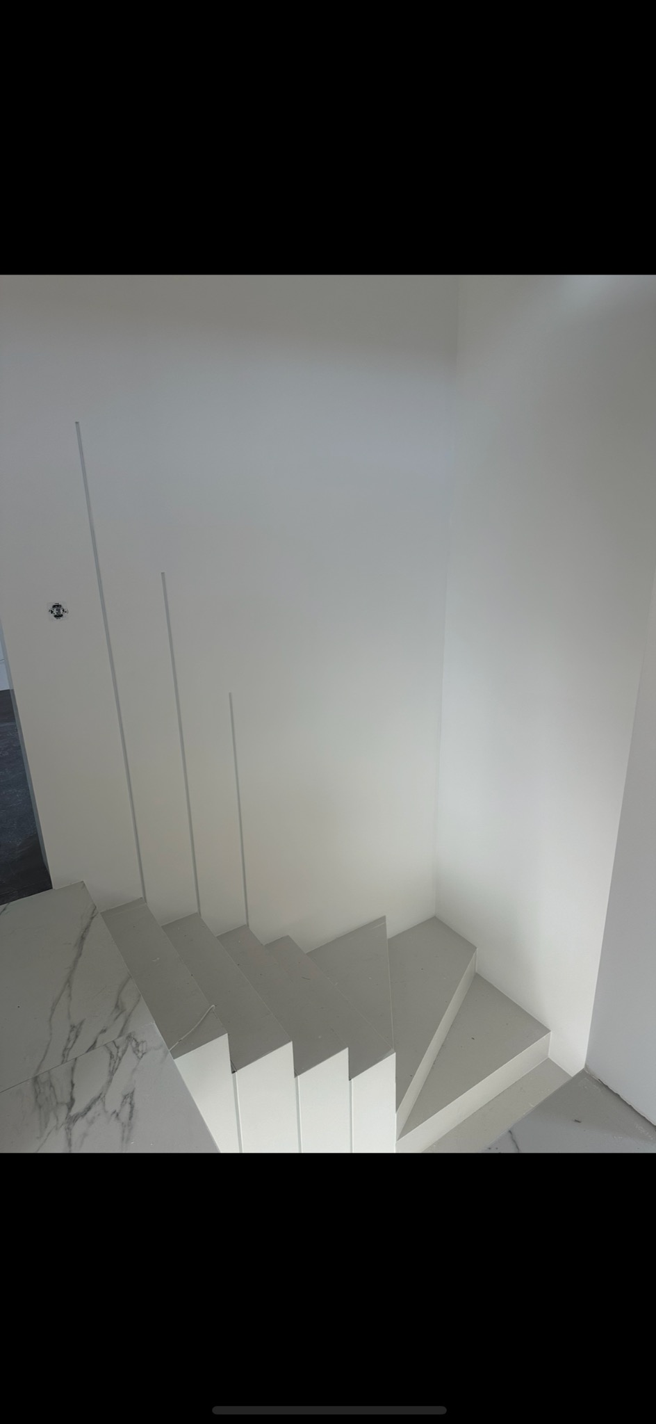 Nowoczesne, białe schody z marmurowym podestem, widok z góry, minimalistyczne wykończenie ścian z subtelnymi pionowymi wgłębieniami.