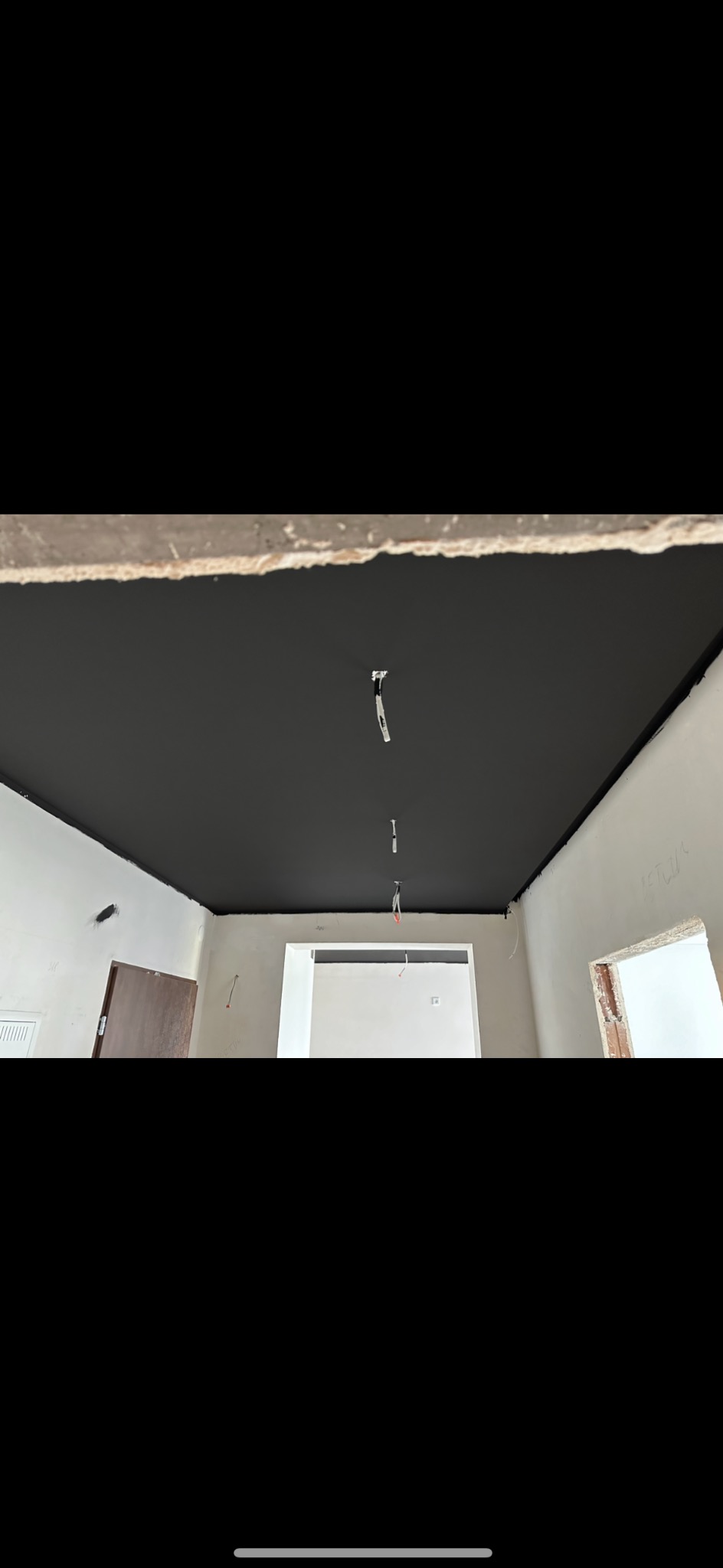 Pomieszczenie w trakcie prac wykończeniowych, sufit pomalowany na czarno, ściany w kolorze białym, widoczne przewody elektryczne.