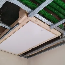 Zamknięty właz na poddasze z płytą kartonowo-gipsową w metalowej konstrukcji sufitu podwieszanego, widoczne zielone rury wentylacyjne