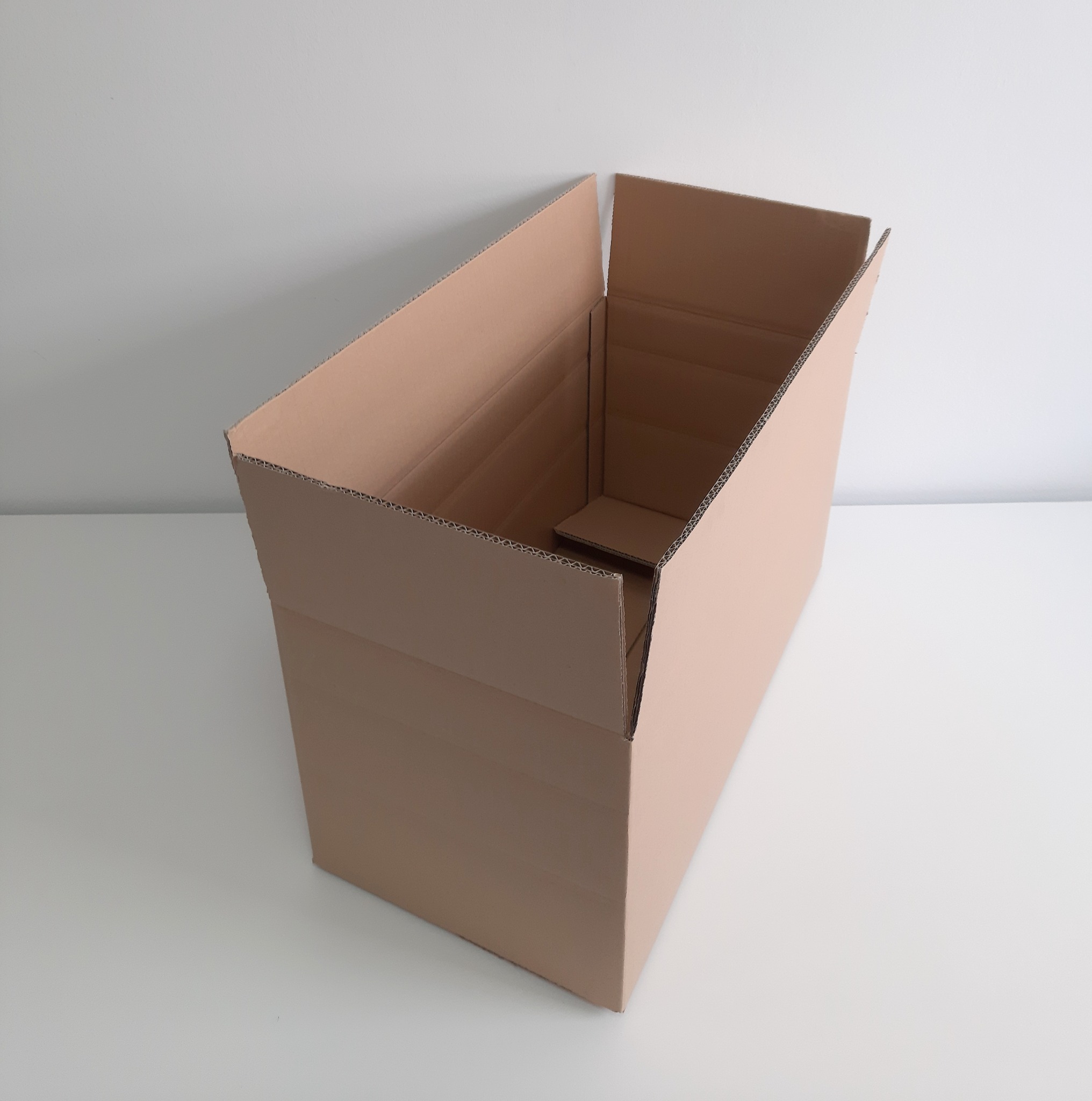 Otwarty, pusty karton z tektury falistej w kolorze naturalnego brązu, widok z góry pod kątem, ukazujący wewnętrzną konstrukcję dna.