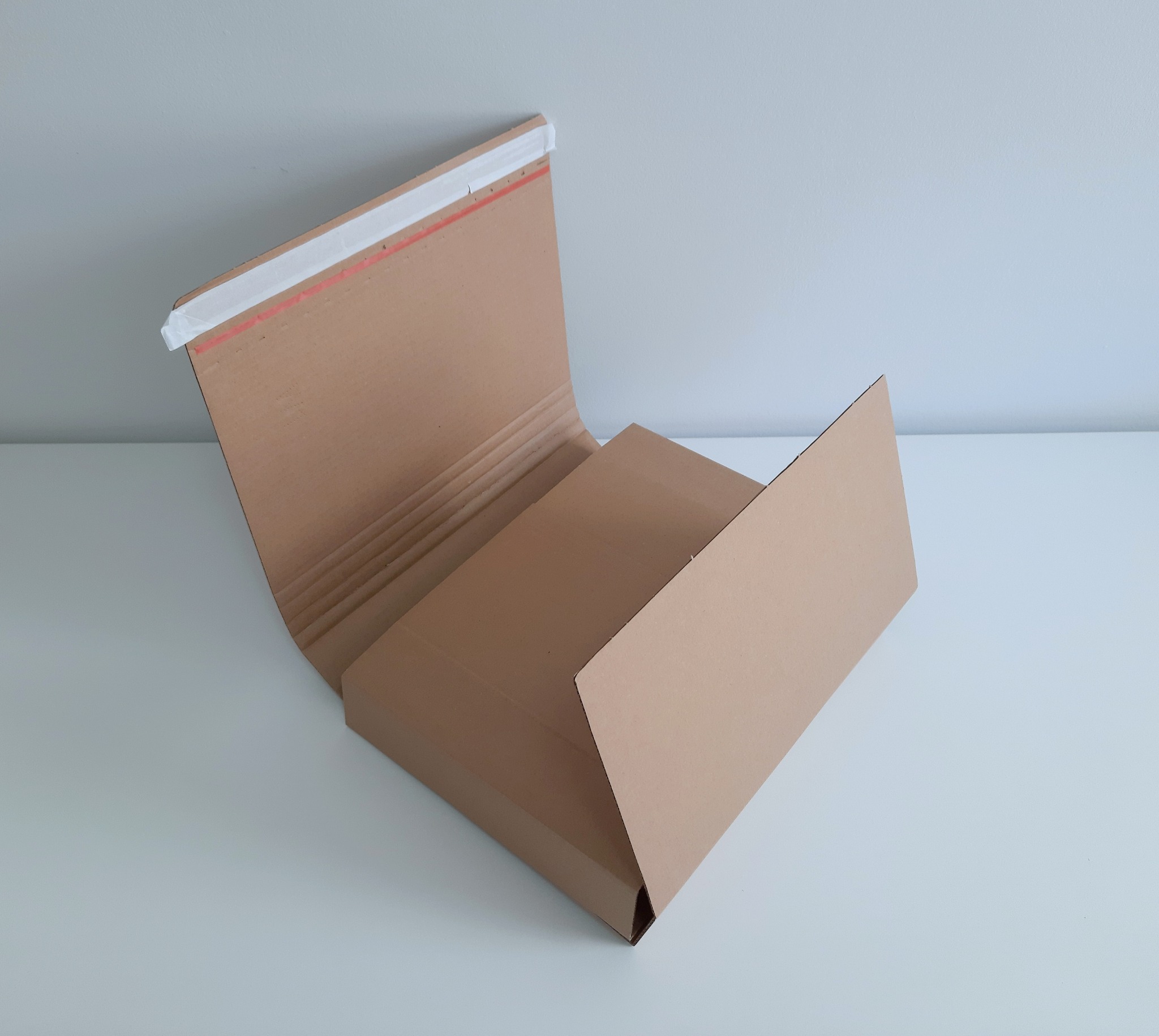 Rozłożone, tekturowe pudełko z widocznym paskiem klejącym i wewnętrzną strukturą falistą, leżące na białym tle.