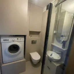 Nowoczesna łazienka z pralką w zabudowie, umywalką nablatową i kabiną prysznicową z czarnymi profilami.