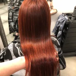 Proste, lśniące włosy w odcieniu miedzianej czerwieni, widok z tyłu, klientka w pelerynie ochronnej z motywem fryzjerskim.