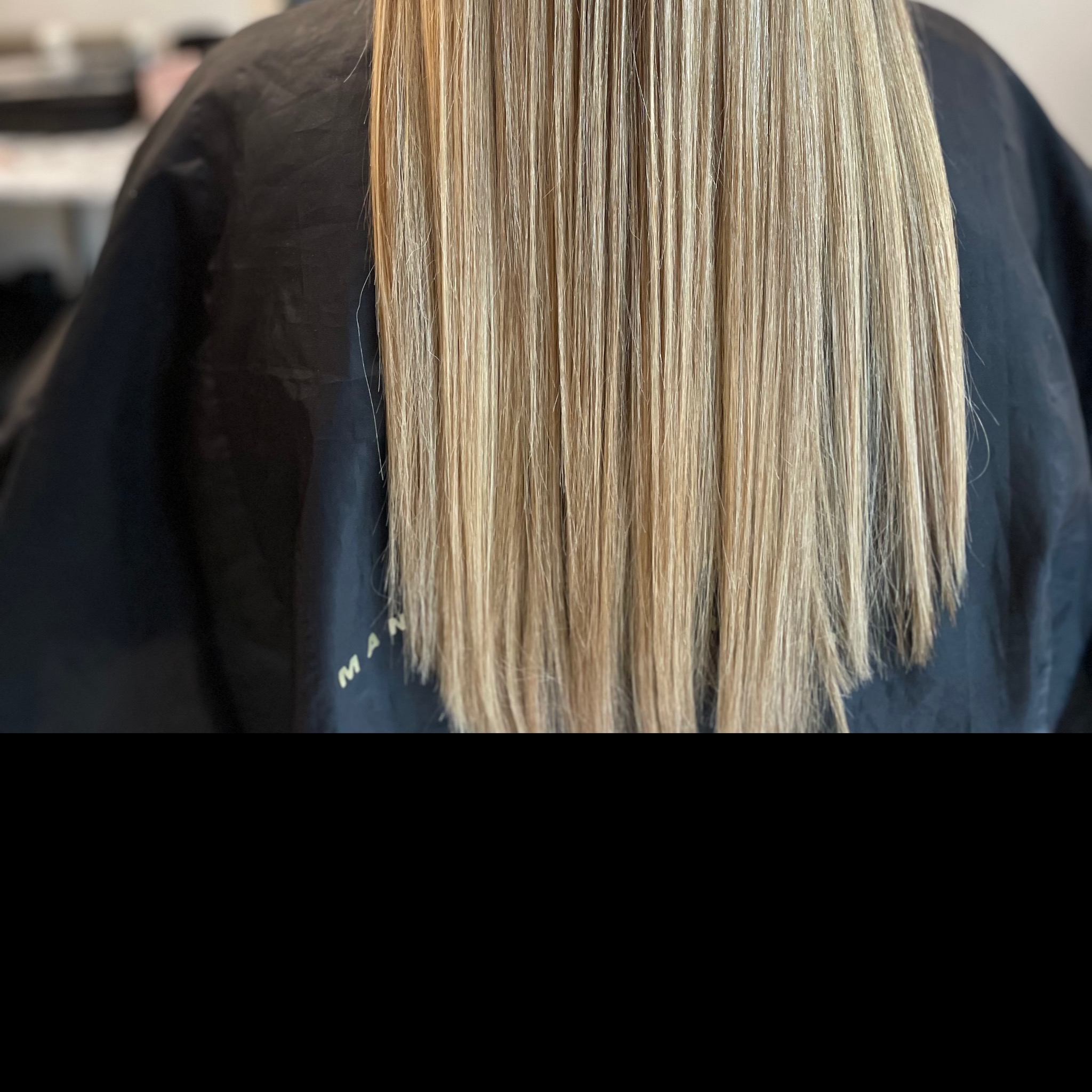 Proste, blond włosy po koloryzacji i strzyżeniu, widoczne od tyłu na tle czarnej peleryny fryzjerskiej.