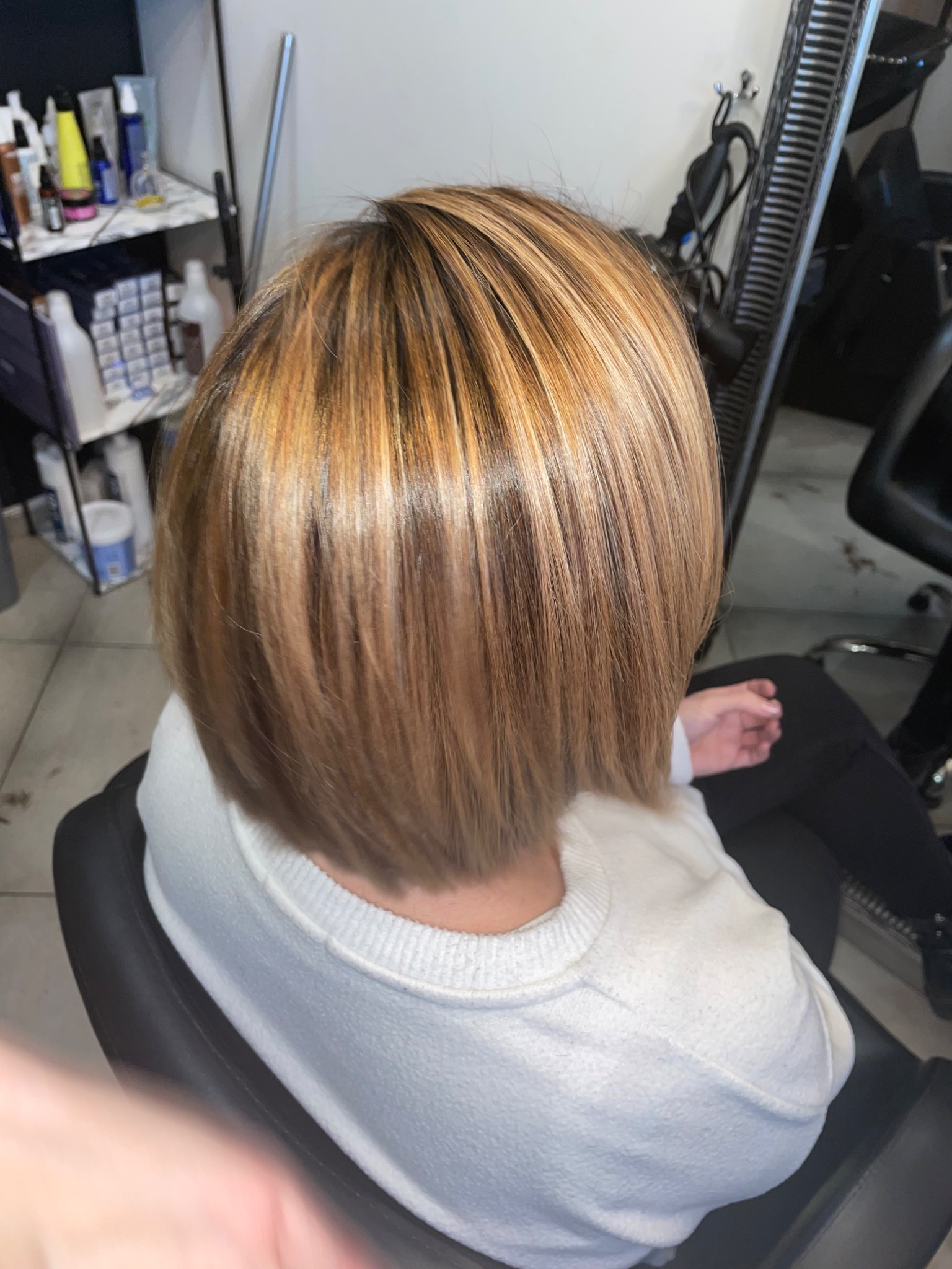 Krótkie, proste włosy z koloryzacją sombre, widoczne od tyłu, w tle półki z kosmetykami.