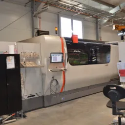 Nowoczesna maszyna CNC Fiber 10000 marki Bystronic w hali produkcyjnej, z widocznym panelem sterowania, szafką narzędziową i elementami wyposażenia stanowiska pracy.