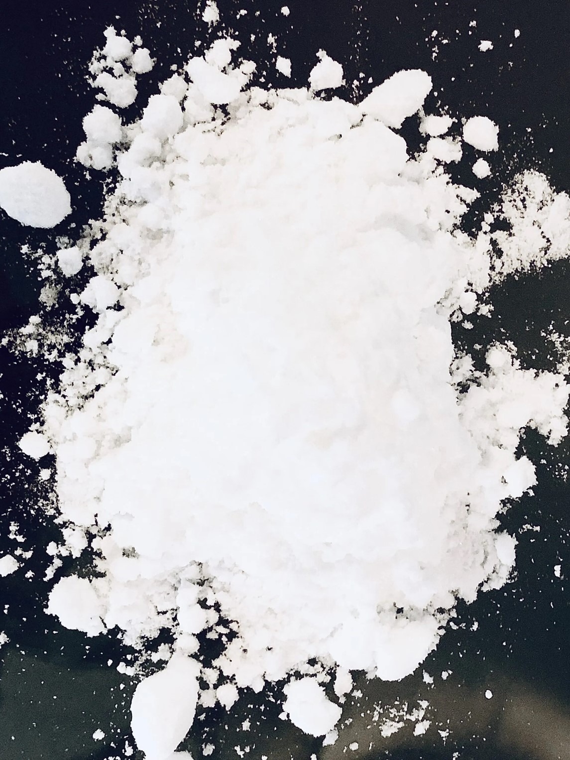 Biały, krystaliczny proszek na ciemnym tle. Nawozy mineralne w formie granulatu, z bliska, tekstura i struktura. Fotografia makro.